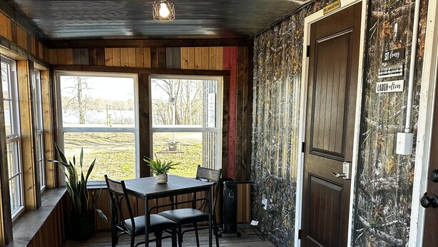 Une pièce chaleureuse avec une table et des chaises en bois, une grande fenêtre et une porte sur laquelle est apposée une pancarte.
