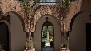 A courtyard with arches, potted plants, and a view of a pool. - Villa Al Assala La Palmerale (Marrakech)
