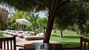 A poolside area with lounge chairs and a table, surrounded by greenery and palm trees. - Villa Al Assala La Palmerale (Marrakech)