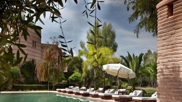 A pool area with lounge chairs and umbrellas, surrounded by palm trees and a building. - Villa Al Assala La Palmerale (Marrakech)