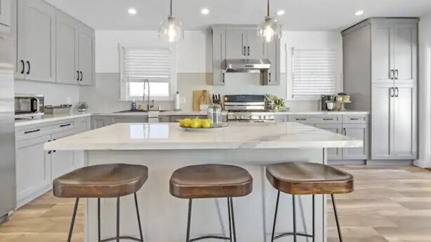 A modern kitchen with a large island, bar stools, pendant lights, and stainless steel appliances.