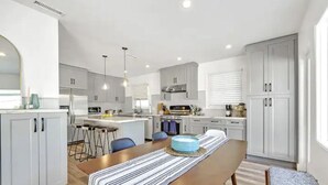 A modern kitchen with white cabinets, a central island, and a dining area with a striped tablecloth.