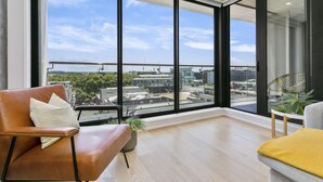 A modern living room with large windows, a leather sofa, a grey armchair, and a small table with a plant. - Laid back living with city views (Auckland)