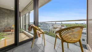 A modern balcony with a view of the city, a wooden chair, and a bench. - Laid back living with city views (Auckland)