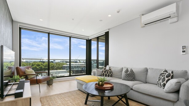 A modern living room with a grey sofa, a black coffee table, and a large window offering a city view. - Laid back living with city views (Auckland)