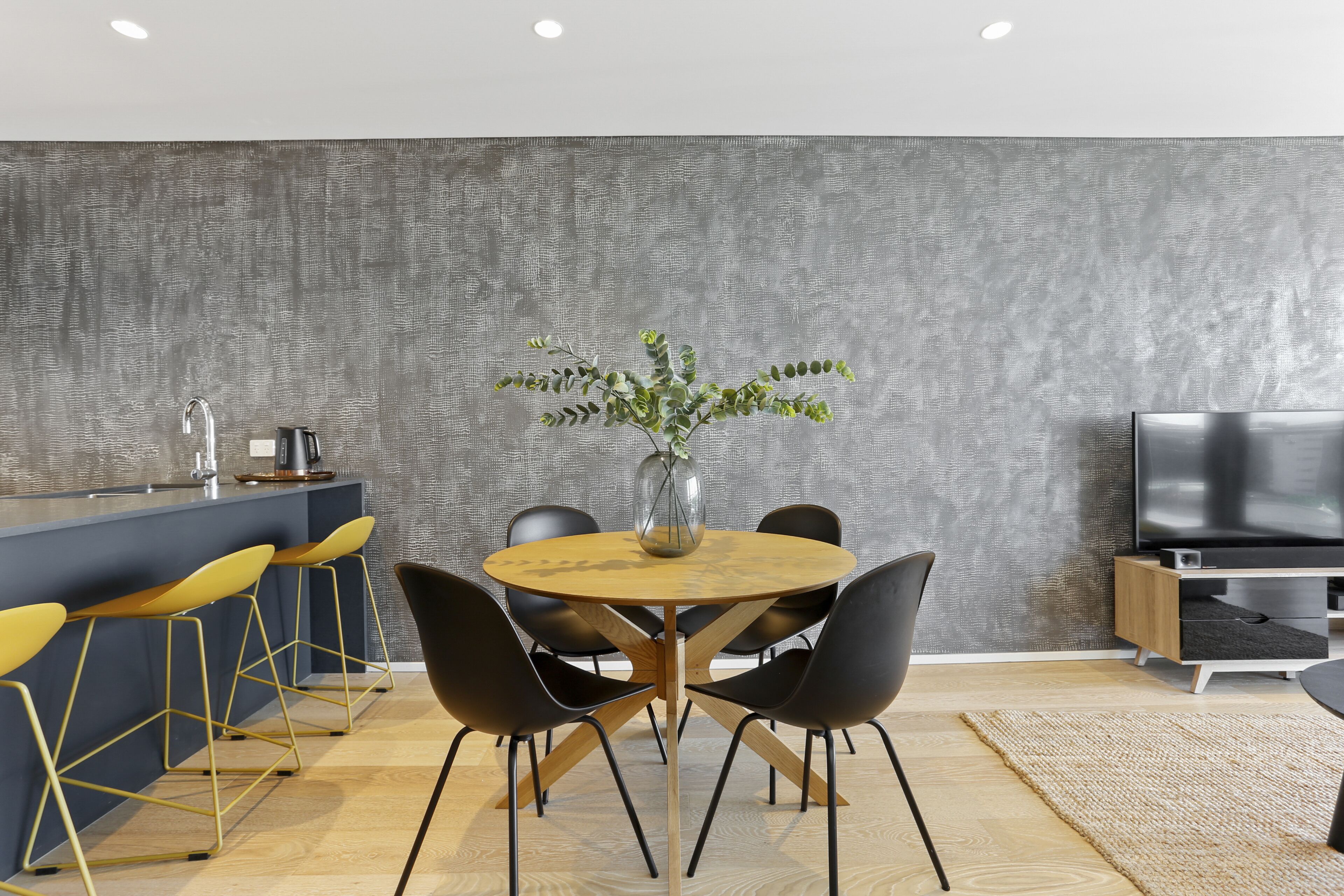 A modern kitchen with a central island, bar stools, and a dining table with chairs.
