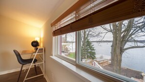 Une pièce comprenant un bureau, une chaise et une fenêtre donnant sur un lac et des arbres.