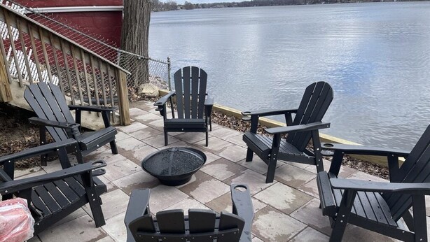 Une terrasse avec des fauteuils Adirondack et un foyer extérieur, le tout offrant une vue sur un lac.