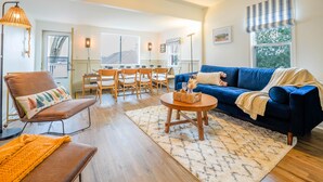 Un salon chaleureux avec un canapé bleu, un fauteuil en cuir marron, une table basse en bois et un coin repas comprenant une table et des chaises.