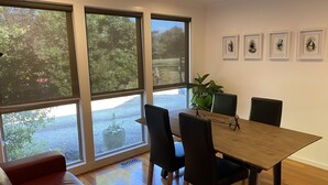 Ein moderner Essbereich mit einem Holztisch, schwarzen Stühlen und einem roten Sofa. Große Fenster bieten einen Ausblick ins Freie.