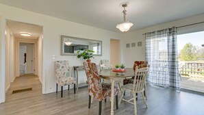 Un coin repas avec une table ronde, des chaises à motifs floraux, un luminaire suspendu et une vue dégagée grâce à de grandes fenêtres ornées de rideaux.