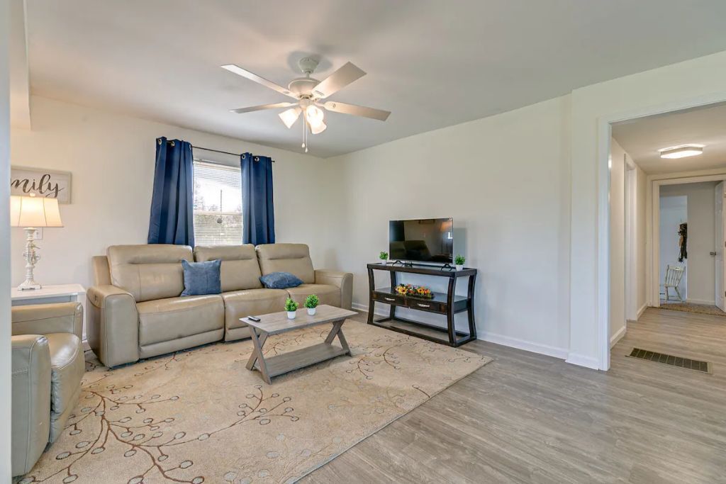A living room with a sofa, coffee table, TV stand, and ceiling fan.