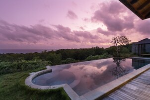 Ein moderner Infinity-Pool mit Holzterrasse, umgeben von üppiger Vegetation und freiem Blick zum Himmel.