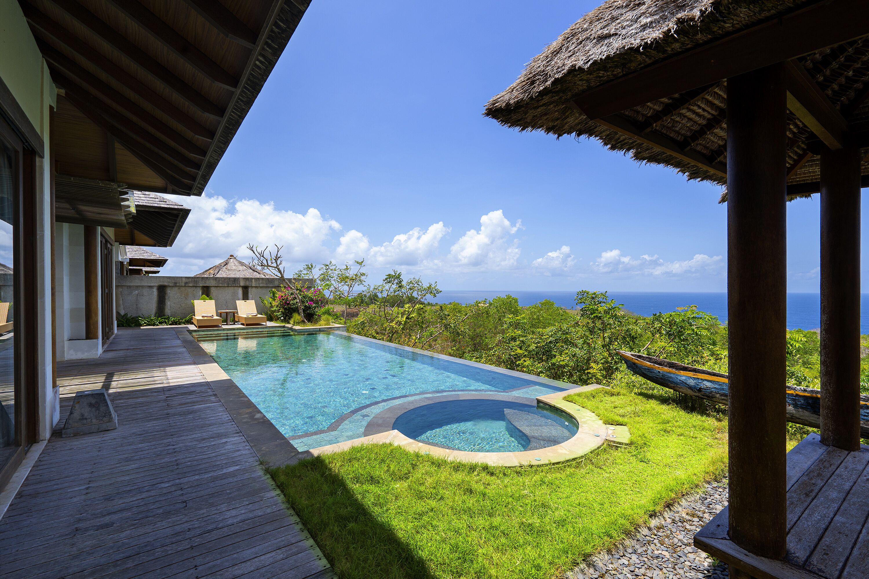 A pool area with a wooden deck, a hot tub, and a view of the ocean.