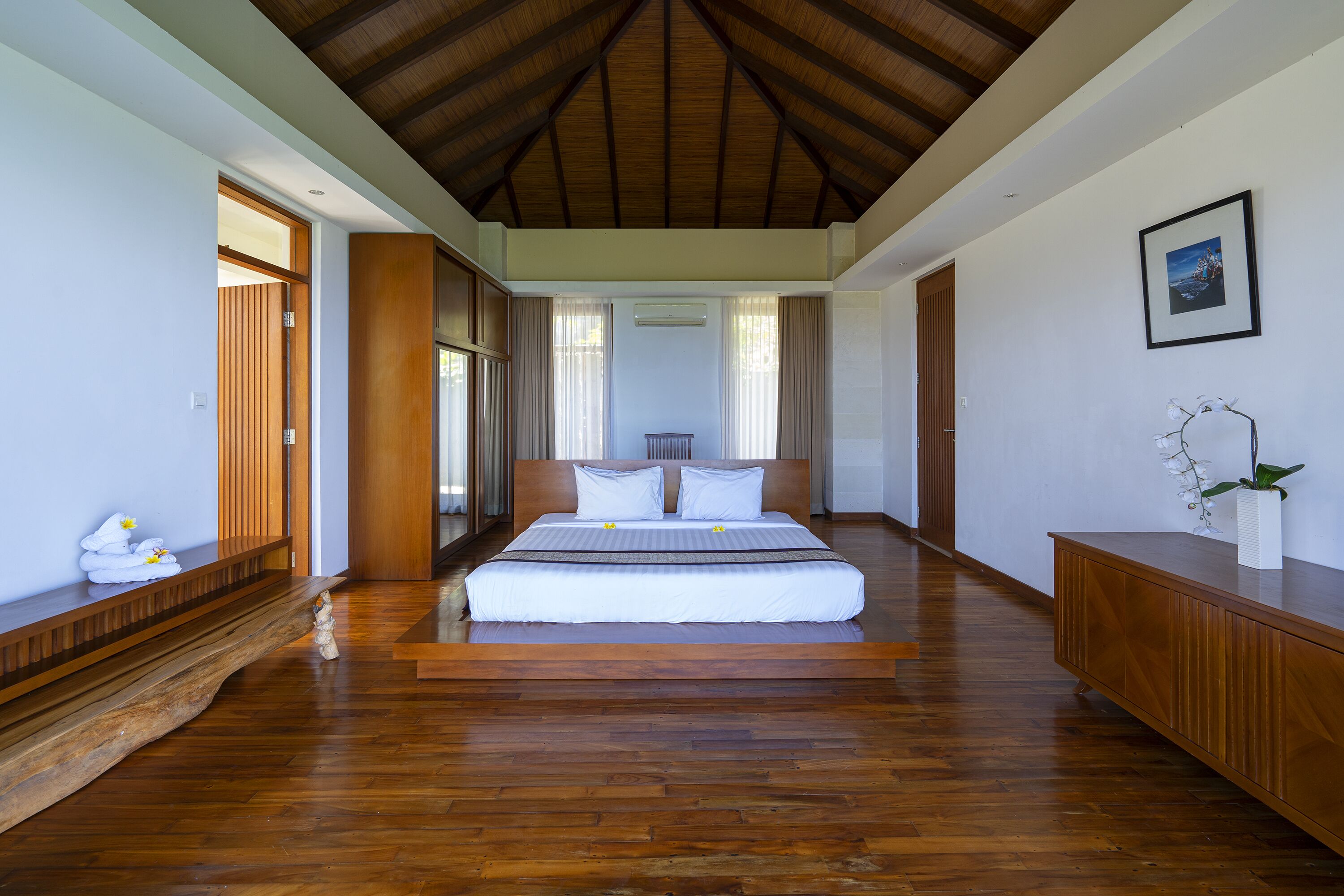 Un dormitorio espacioso con una cama grande, suelo de madera y techo alto.