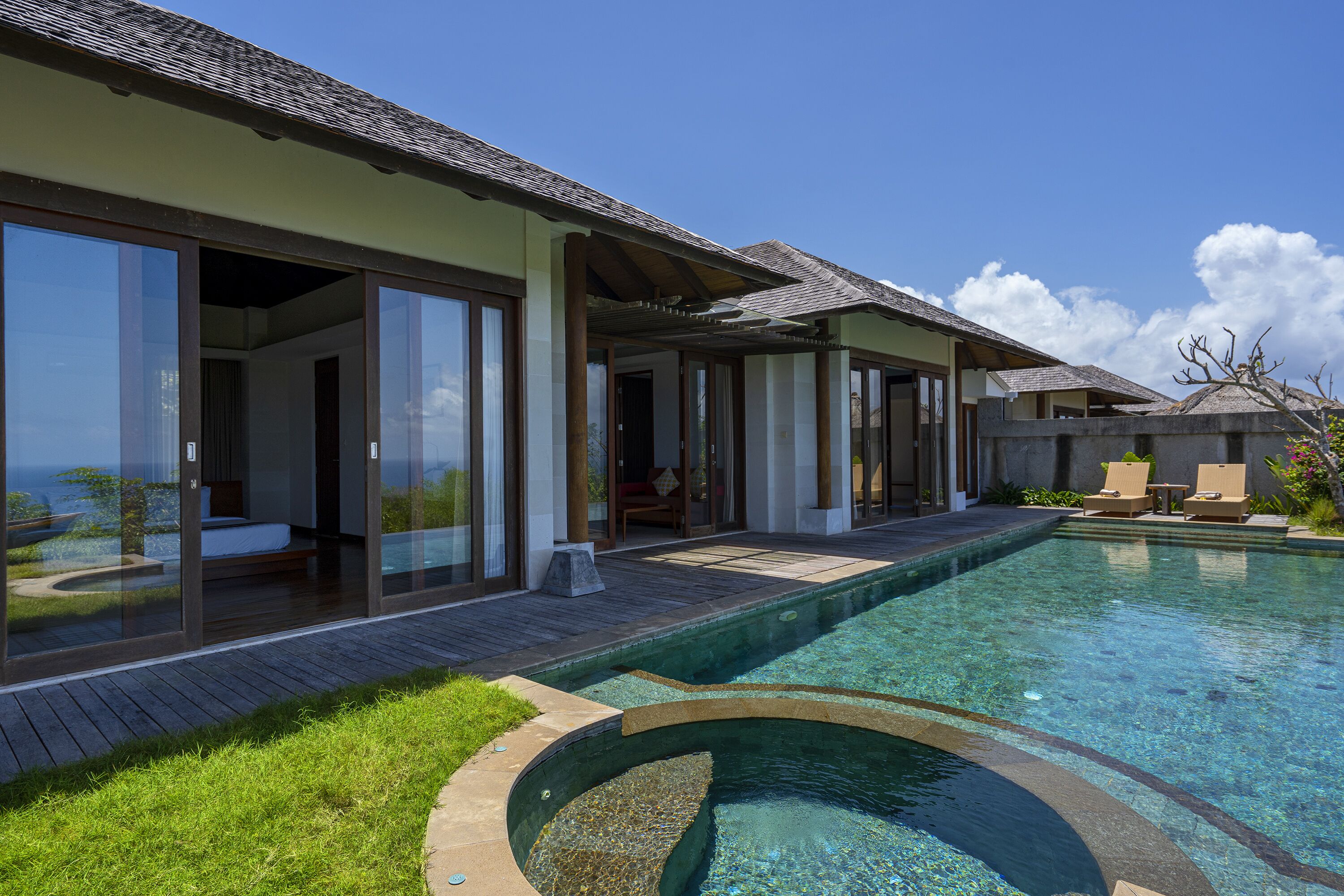 A modern resort with a swimming pool, glass-enclosed rooms, and a view of the ocean.