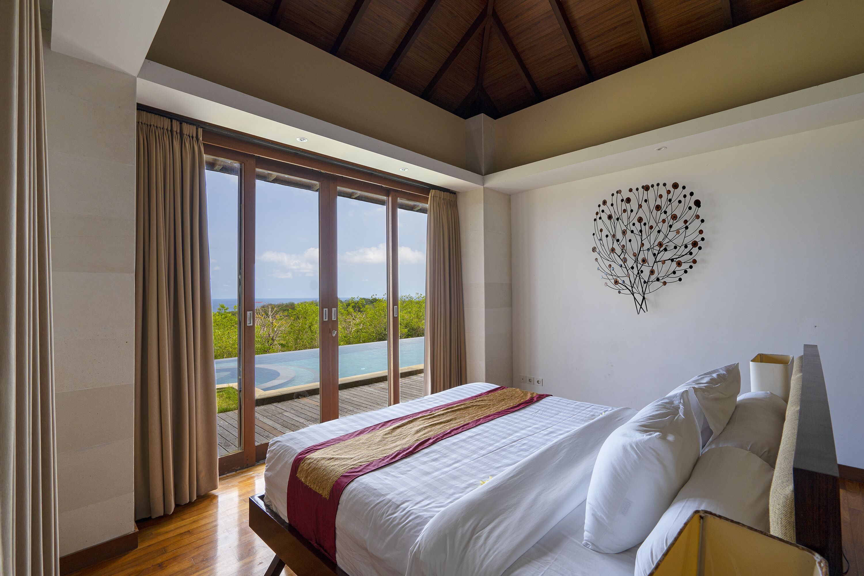 Ein Schlafzimmer mit einem großen Bett, Blick auf einen Pool und einer Decke mit Holzbalken.