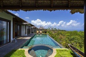 Una piscina con un jacuzzi circular, una terraza de madera y vista al océano.