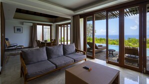 A modern living room with a sofa, a coffee table, and a view of the ocean through large sliding glass doors. - Moritz Palm Villa (Kutuh)