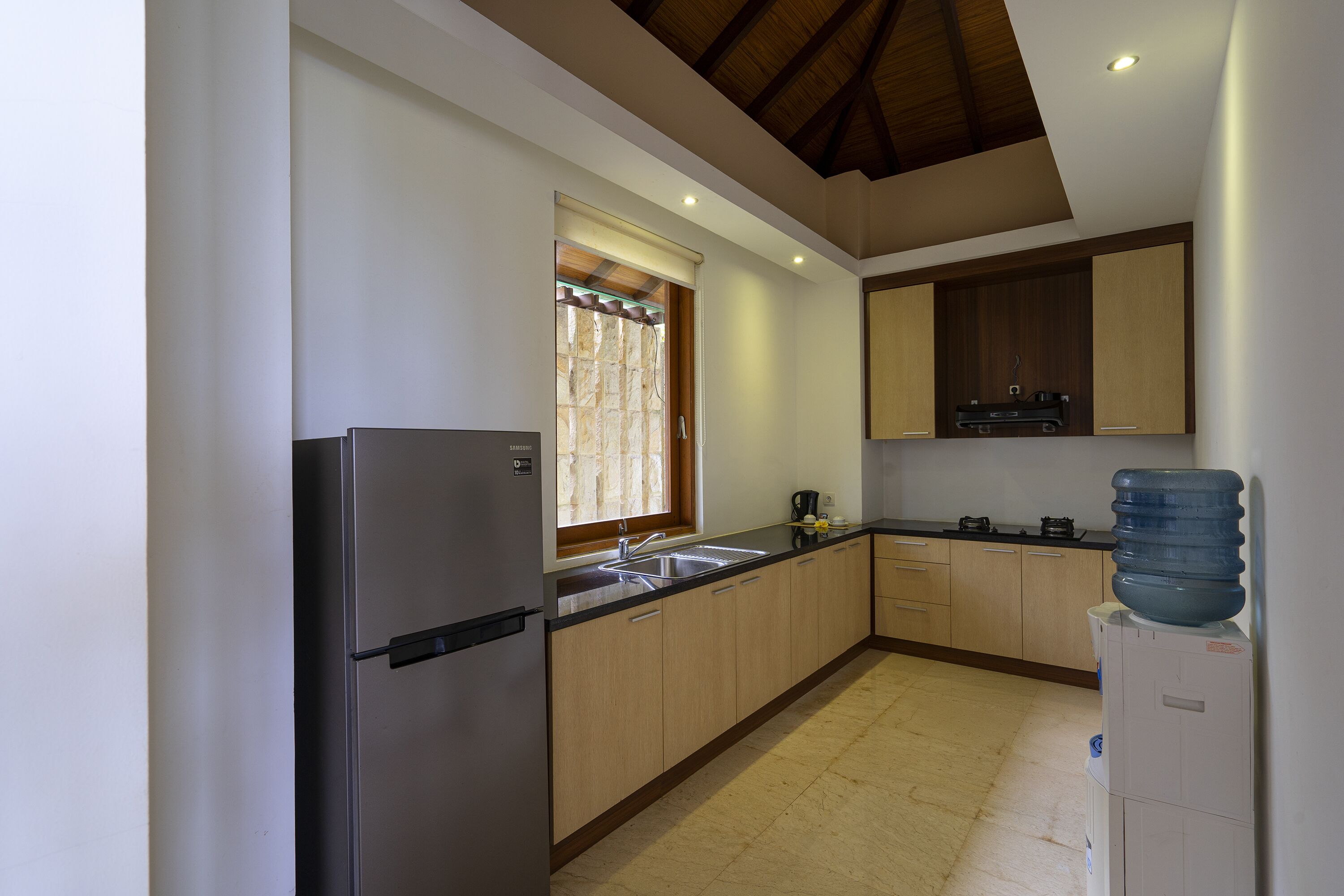 A kitchen with a refrigerator, sink, wooden cabinets, and a water dispenser.