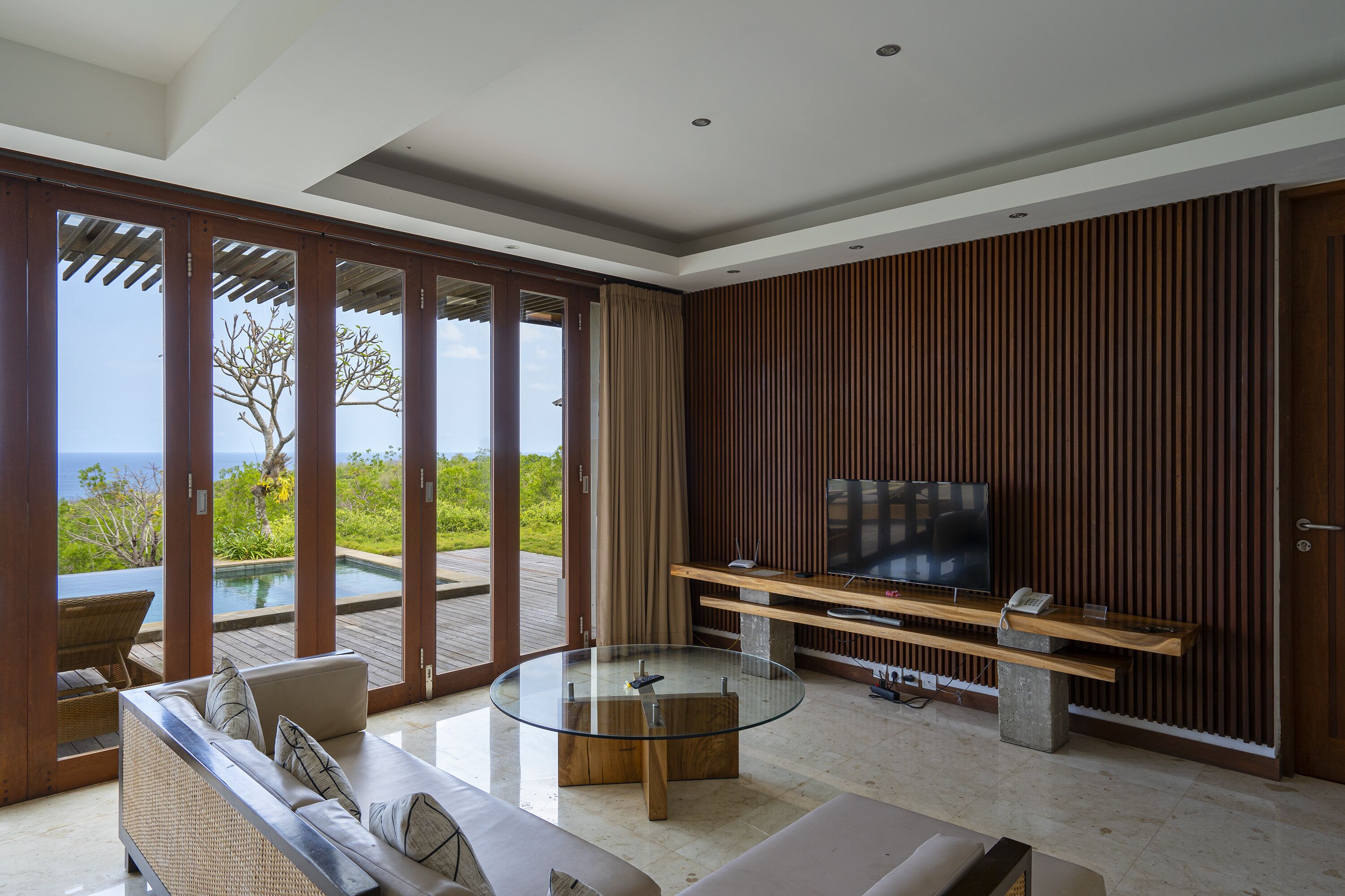 A modern living room with a glass coffee table, a sofa, and a TV on a wooden stand.