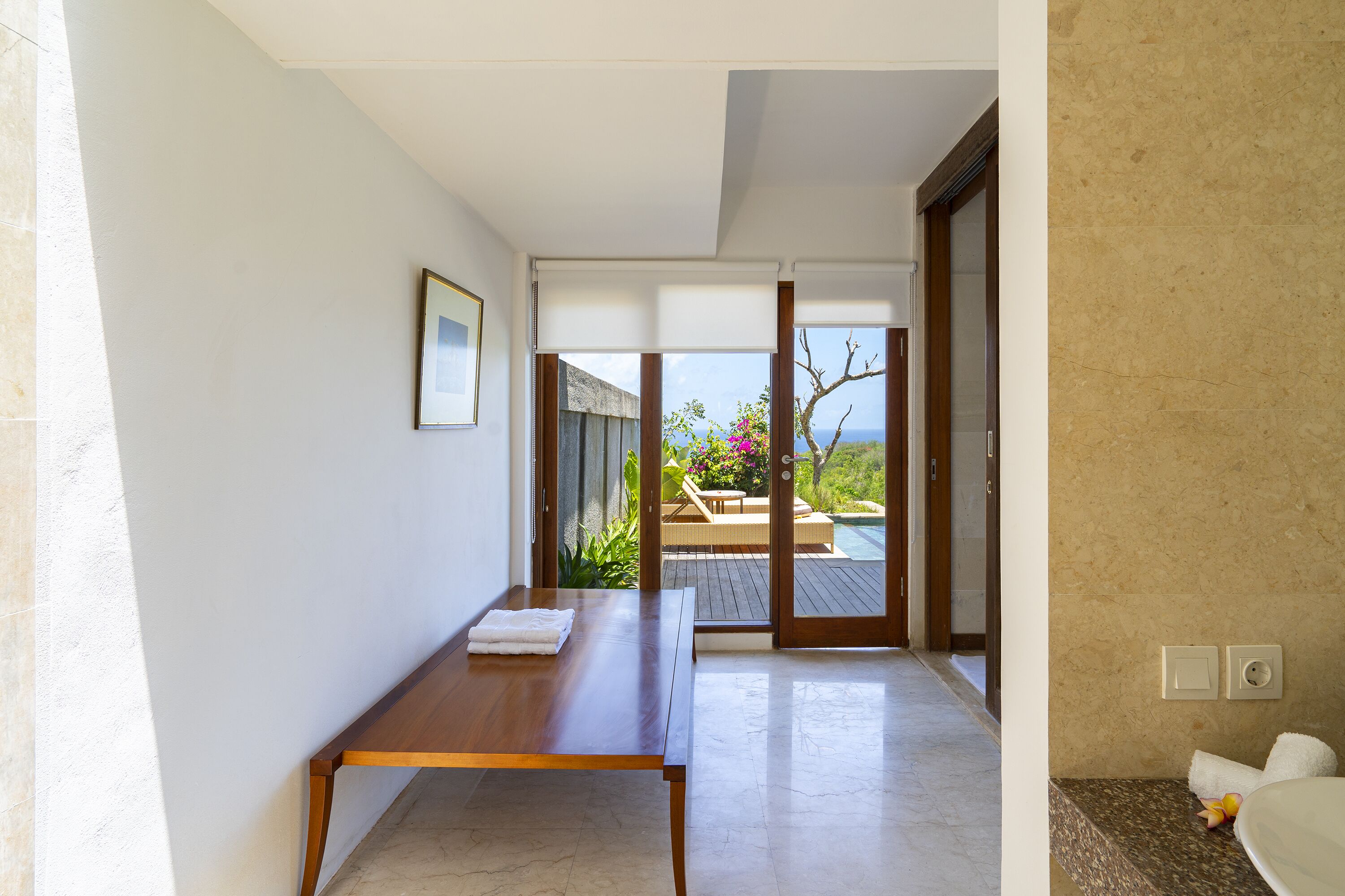 Une chambre d’hôtel moderne avec une table en bois, un tableau encadré au mur et une vue sur l’espace extérieur de la piscine.