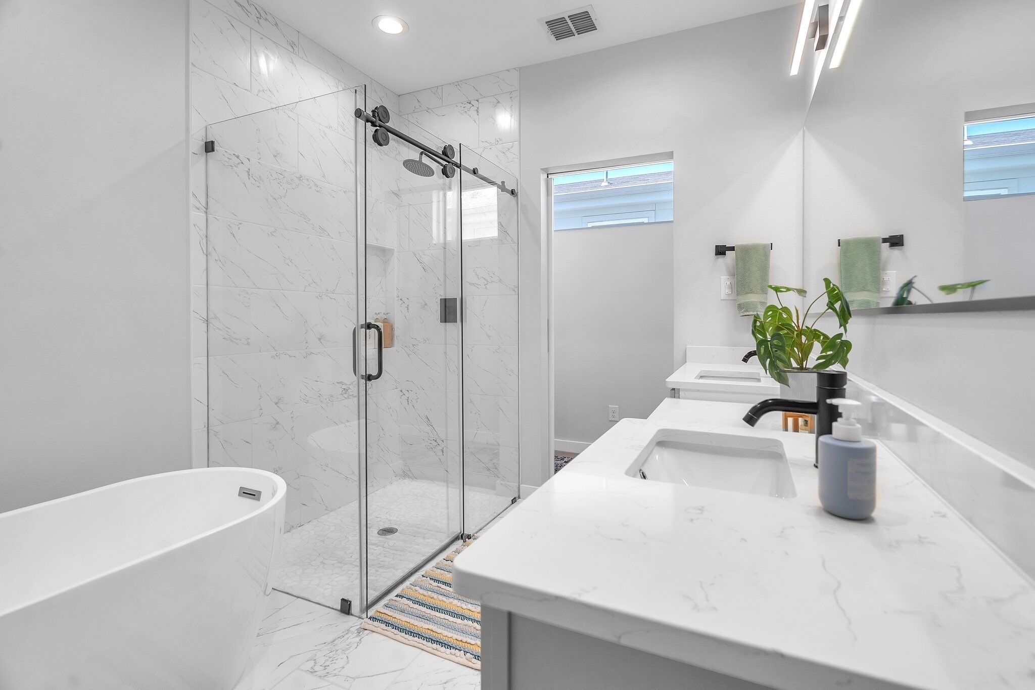 Une salle de bain moderne dotée d’une douche à parois de verre, d’une baignoire sur pieds et d’un meuble-lavabo agrémenté d’un pot de fleurs.