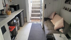 Ein kompakter Wohnbereich mit Küchenzeile, einer Couch, einem kleinen Tisch und einer Treppe, die zu einer erhöhten Ebene führt.
