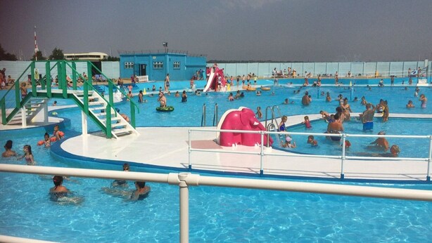 Ein großer Außenpool mit mehreren Bahnen, einer Wasserrutsche und einem Rettungsschwimmerstand.