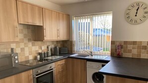 A kitchen with wooden cabinets, a built-in oven, a washing machine, and a clock on the wall. - Cottage - Sleeps 4 - Dog friendly - Parking (Bridlington)