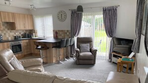 A modern living room with a leather sofa, a dining area with a bar, and a kitchen with wooden cabinets. - Cottage - Sleeps 4 - Dog friendly - Parking (Bridlington)