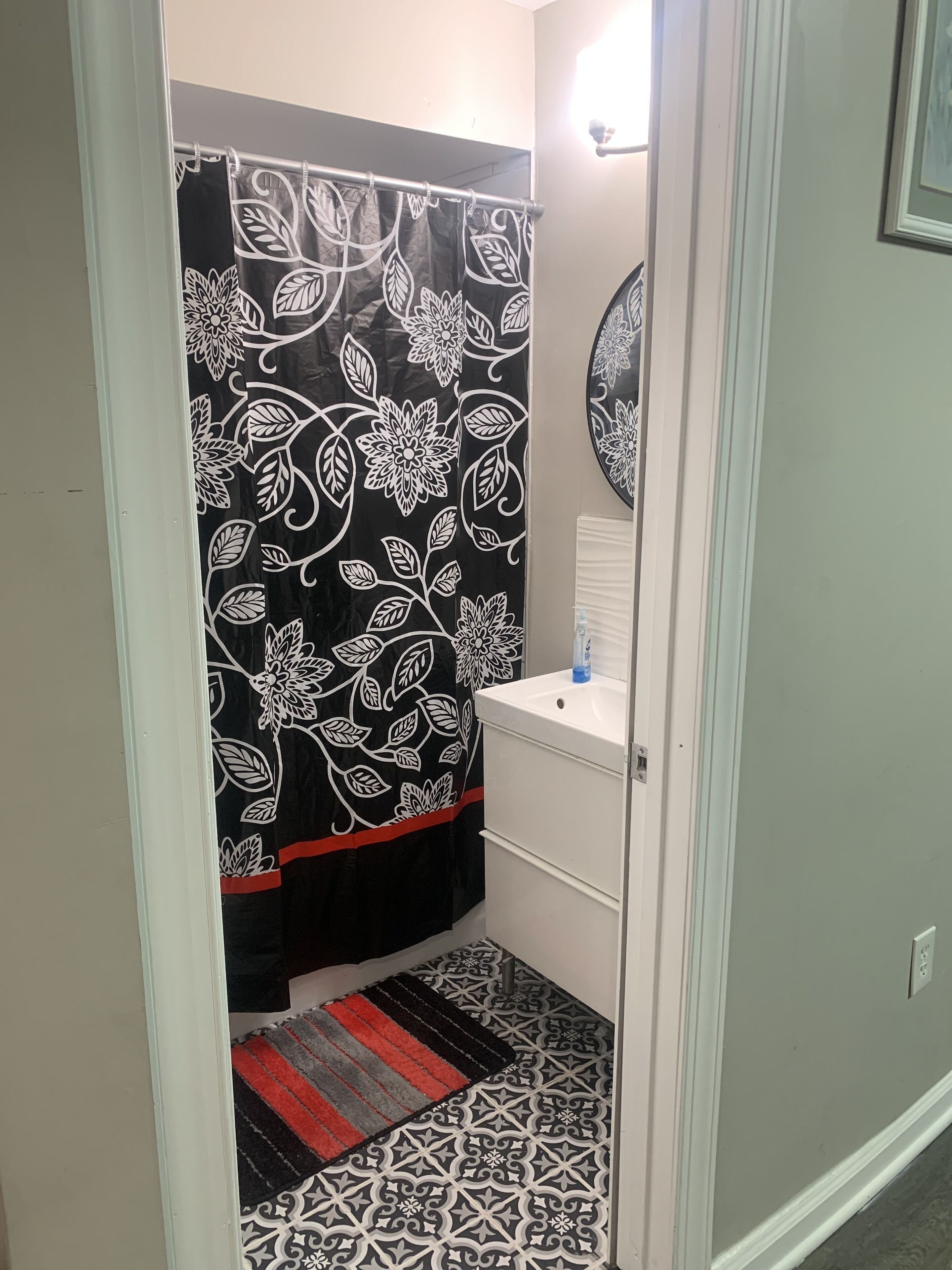 Ein Badezimmer mit einem schwarz-weißen Blumenvorhängen, einem weißen Waschbecken und einem gemusterten Boden.