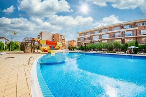 Ein Pool mit Wasserrutsche, umgeben von mehrstöckigen Gebäuden mit Balkonen.
