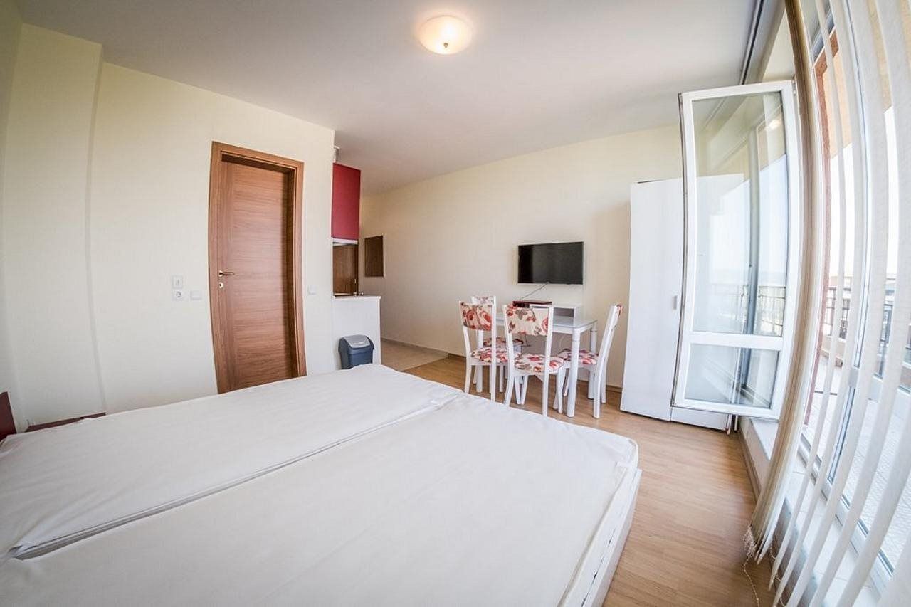 A bedroom with a bed, a desk with a chair, a television, and a window.