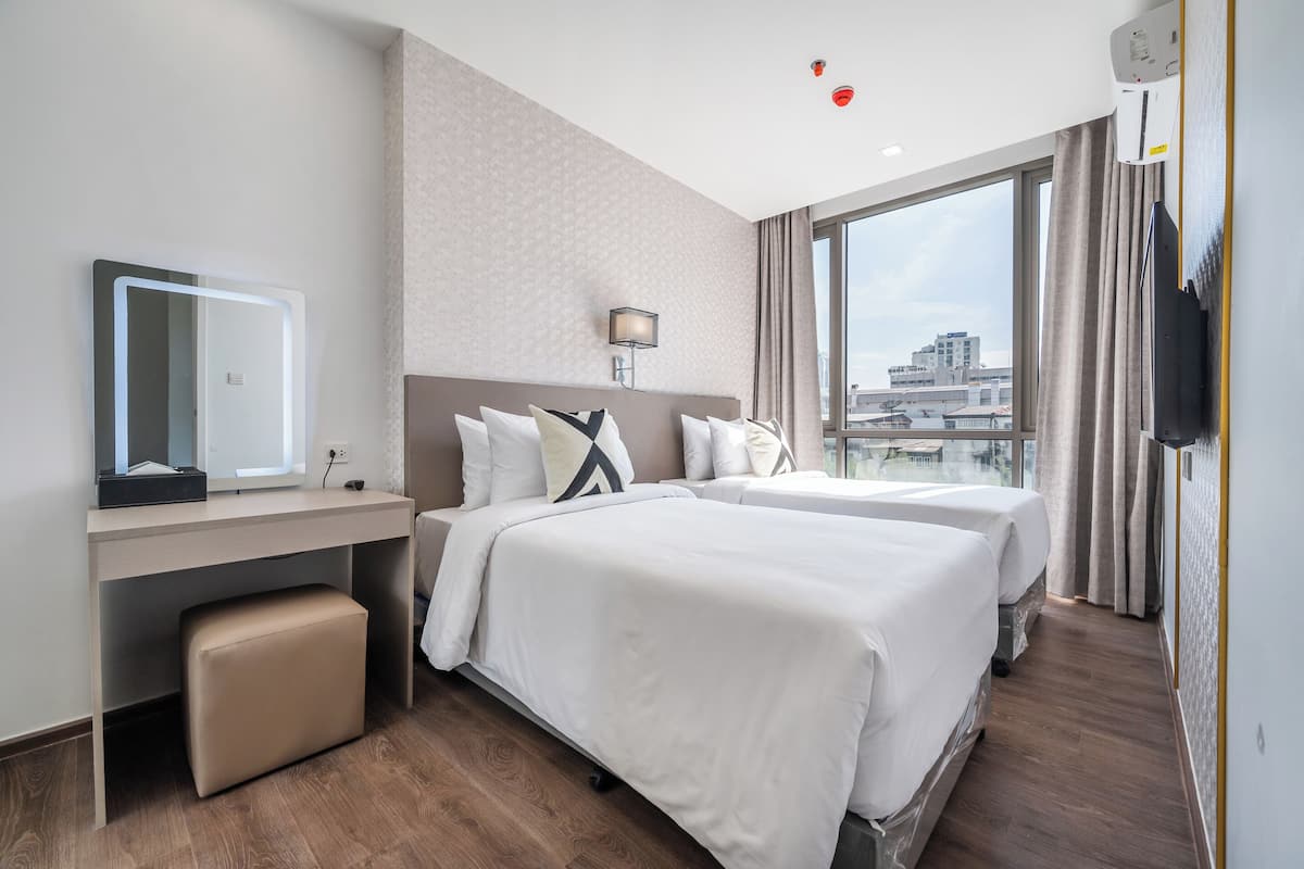 Ein Hotelzimmer mit zwei Betten, einem Schreibtisch mit Spiegel, einem Flachbildfernseher und einem großen Fenster mit Blick auf die Stadt.