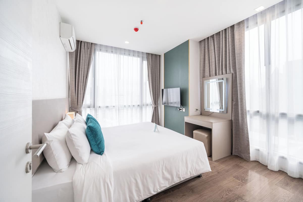 Ein modernes Hotelzimmer mit einem großen Bett, einem Nachttisch, einem Spiegel und einem Fenster mit Vorhängen.