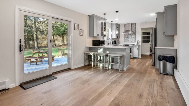 A modern kitchen with a large island, bar stools, and a view of a patio with a picnic table. - Hudson Valley Hilltop Escape w/Hot Tub, 5private acres, near wine trail, orchard (Marlboro)