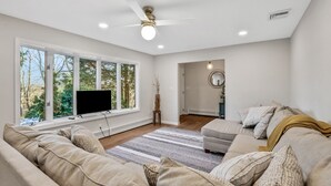 A modern living room with a large window, a ceiling fan, and a flat-screen TV. - Hudson Valley Hilltop Escape w/Hot Tub, 5private acres, near wine trail, orchard (Marlboro)