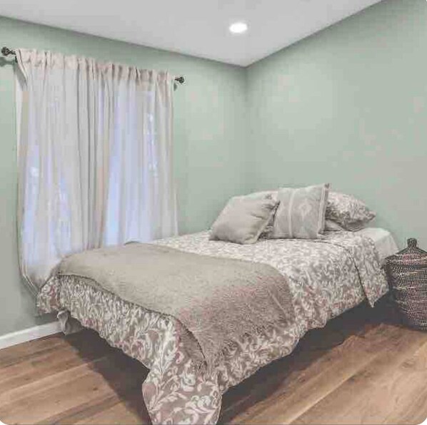 Un dormitorio con cama, cortinas y mesita de noche.
