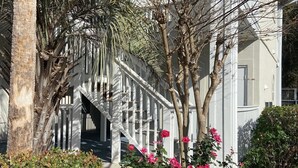 A building with a white exterior, a covered staircase, and a garden with pink flowers and green shrubs. - Quiet Beach Getaway (Myrtle Beach)