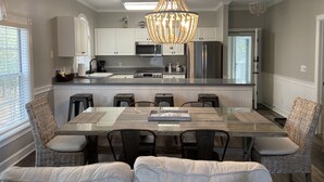 A modern kitchen with white cabinetry, a stainless steel refrigerator, and a glass island with bar stools. - Quiet Beach Getaway (Myrtle Beach)