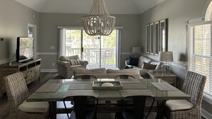 A spacious dining area with a glass table, wicker chairs, and a central chandelier. - Quiet Beach Getaway (Myrtle Beach)