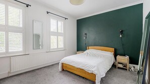 A bedroom with a wooden bed, white bedding, a green accent wall, and a window with blinds. - Inviting 3-bed House in Beckenham (Beckenham)