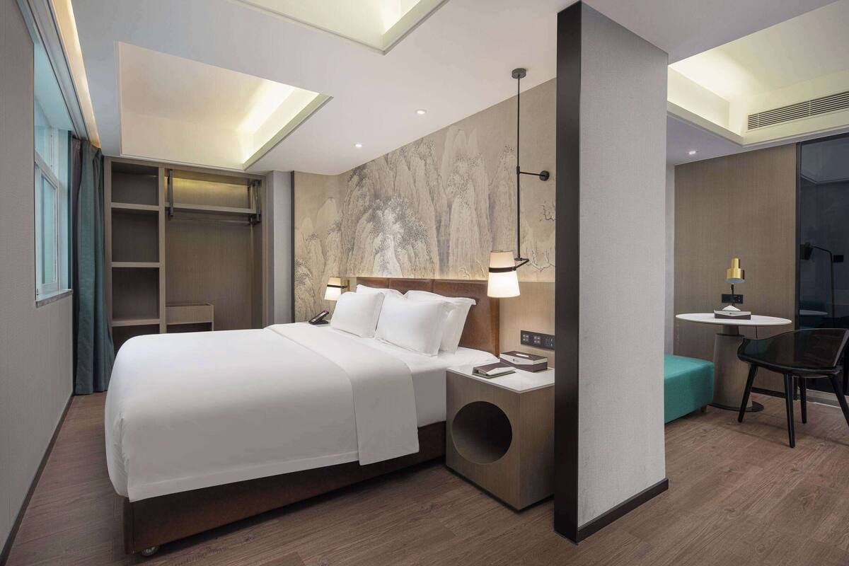 A modern hotel room with a large bed, bedside tables, a desk, and a chair.