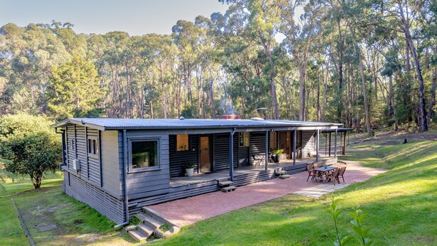 Een modern huis met een overdekte veranda, een terras met tuinmeubilair en uitzicht op een bebost gebied.