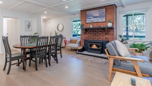 Een ruime woonkamer met een open haard, een eethoek met houten stoelen en een groot raam dat zorgt voor daglicht.