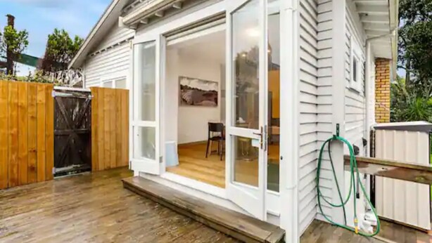 A house with a covered porch, a wooden deck, and a garden hose.