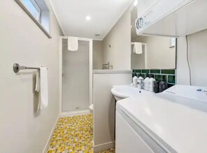 A bathroom with a shower, a sink with toiletries, and a mirror. - Lovely 3-Bedroom Home With Free Parking (Auckland)