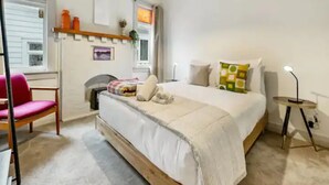 A bedroom with a bed, a chair, a bedside table, and a window.