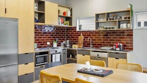 A modern kitchen with a brick backsplash, stainless steel appliances, wooden cabinets, and a dining area with a table and chairs.
